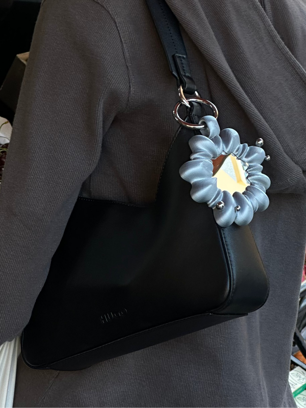 Person with a black handbag featuring a decorative flower detail, standing in front of a fruit stand.