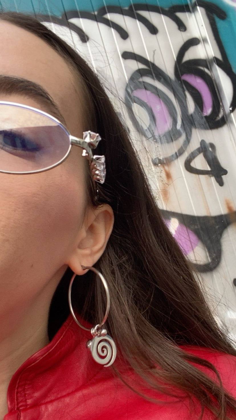 Person wearing glasses with decorative frames and a red jacket, with big spiral hoop earrings
