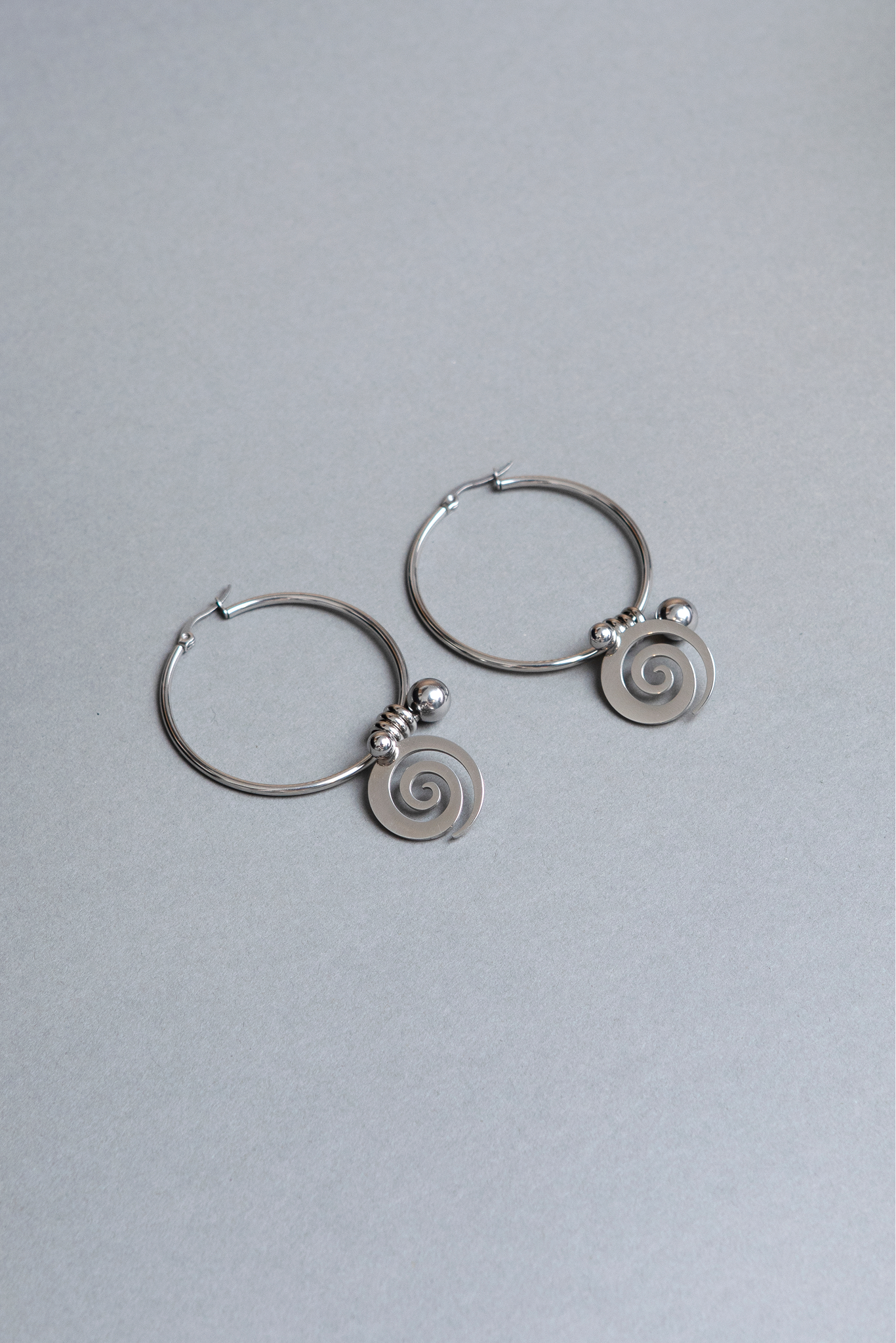 Pair of silver hoop earrings with spiral designs on a light gray background