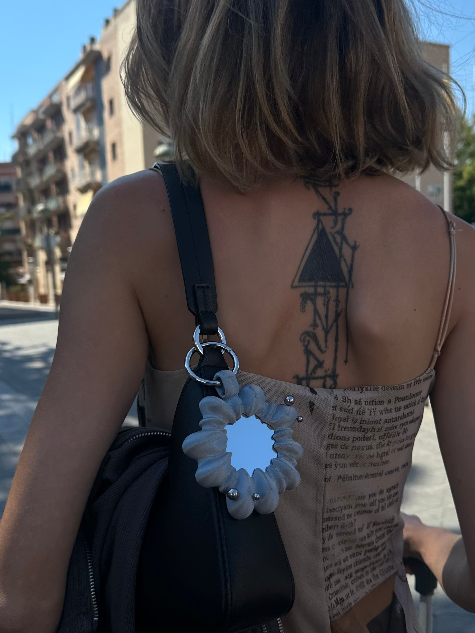 Person with a tattoo on their back walking outdoors on a sunny day.