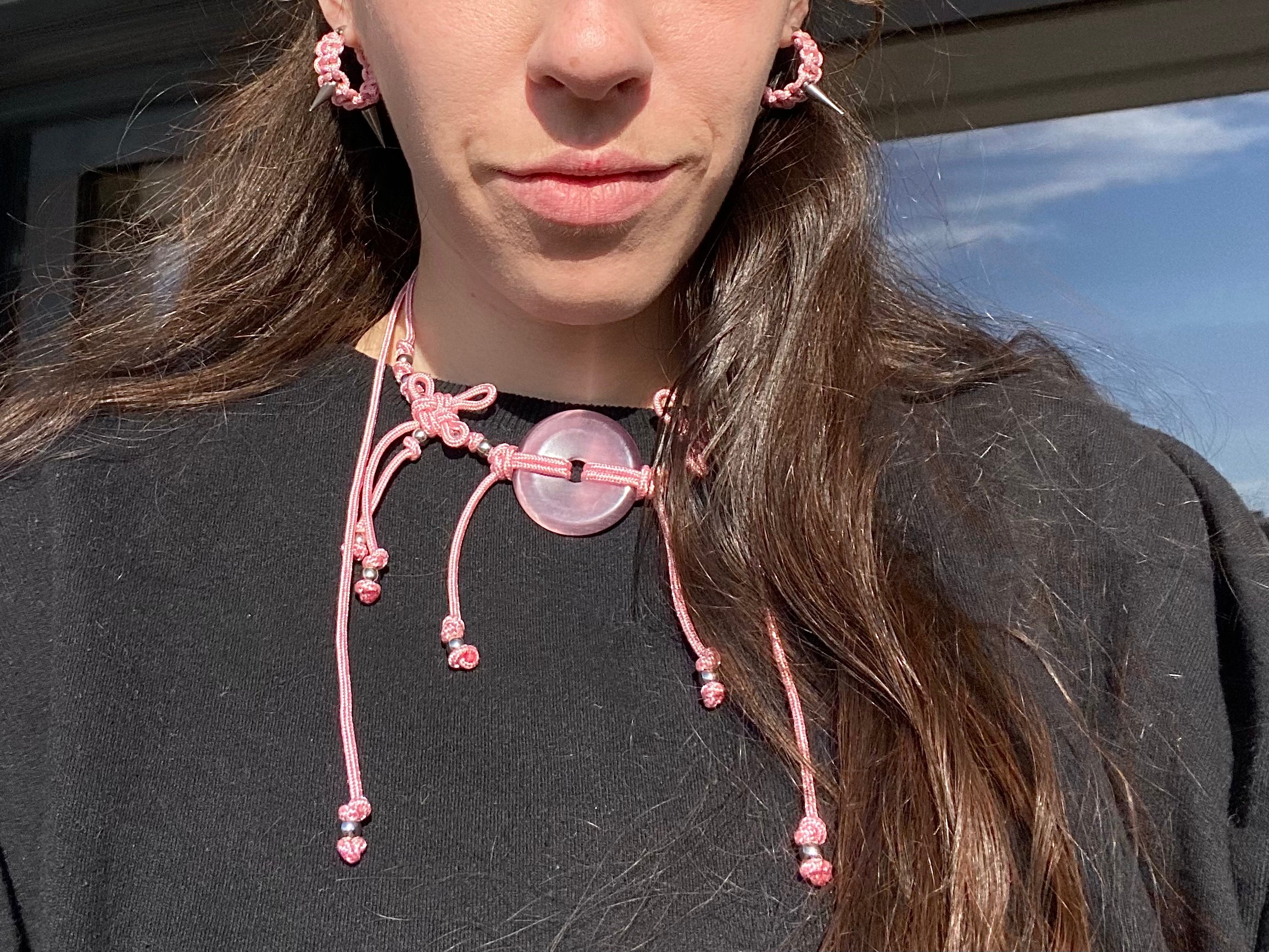 Person wearing a pink beaded necklace and earrings outdoors