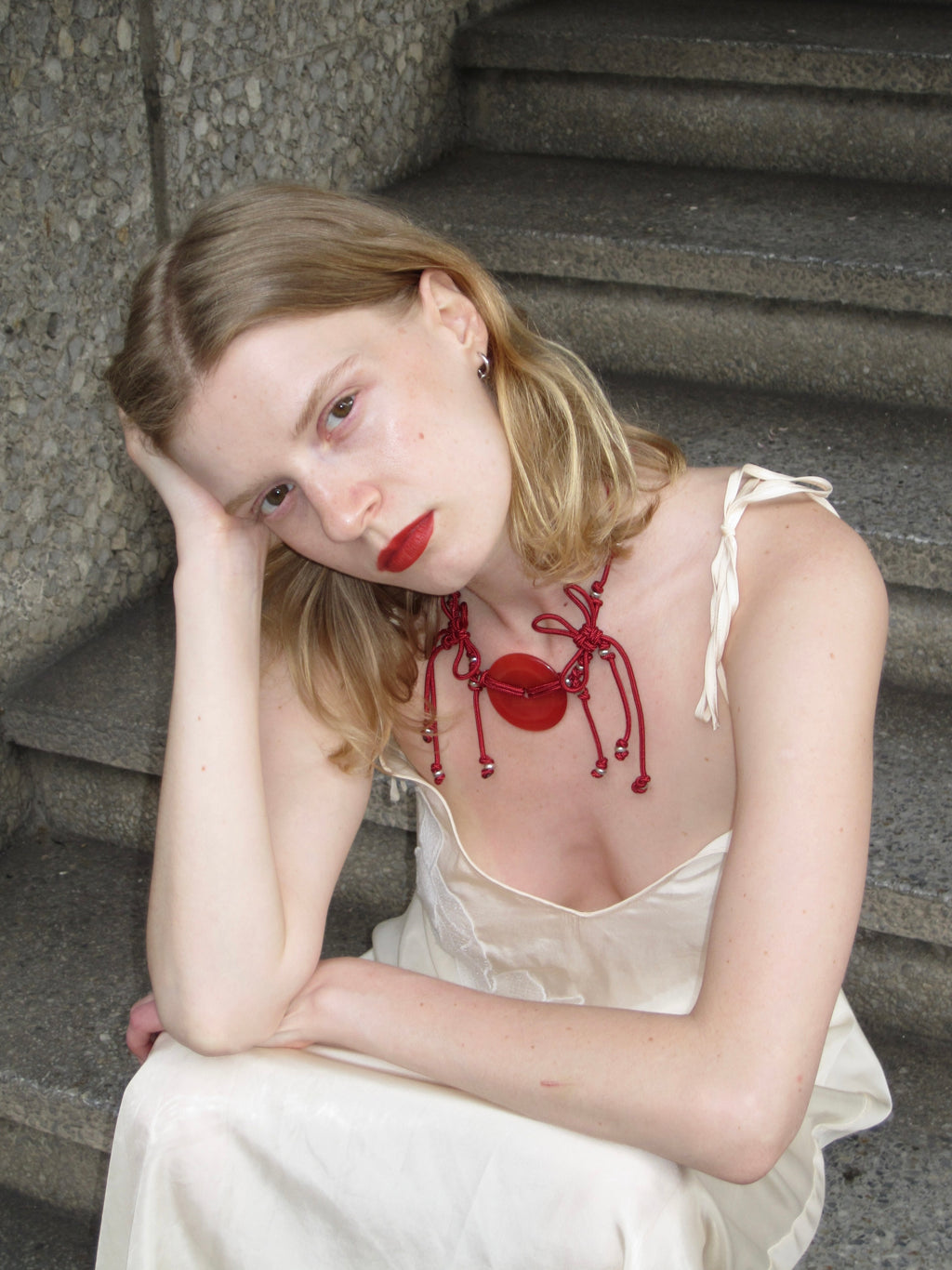 Woman sitting on steps wearing a white dress with a red necklace
