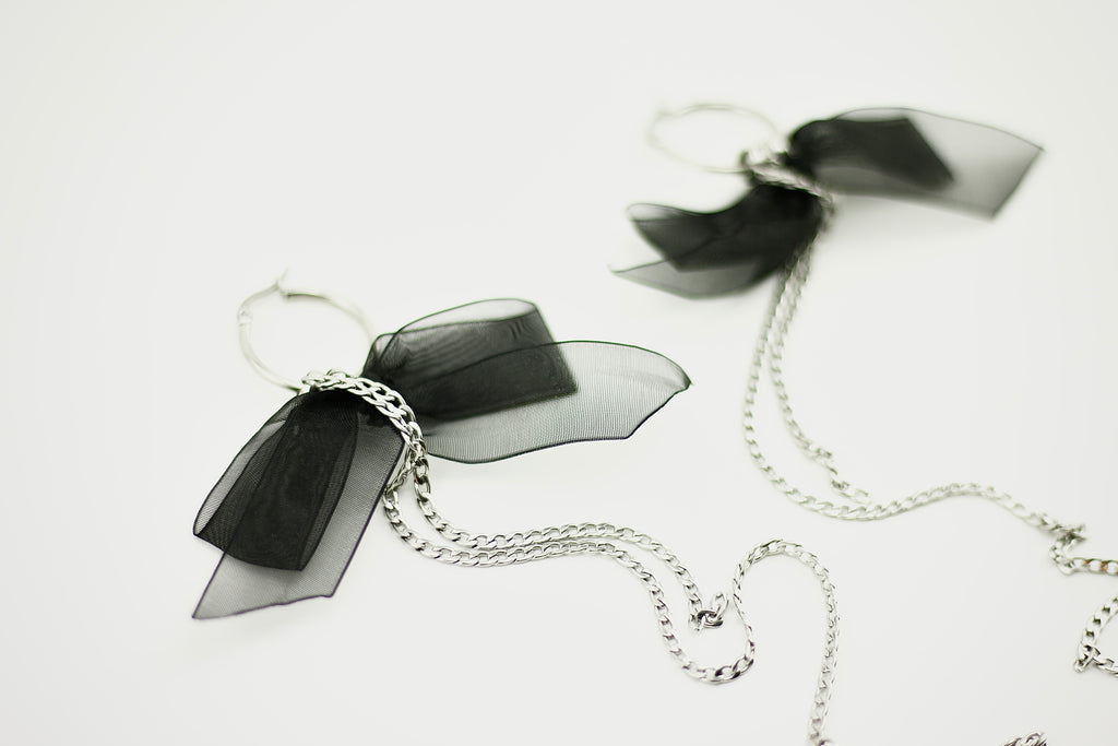 Black bow-shaped earrings with silver chains on a white background