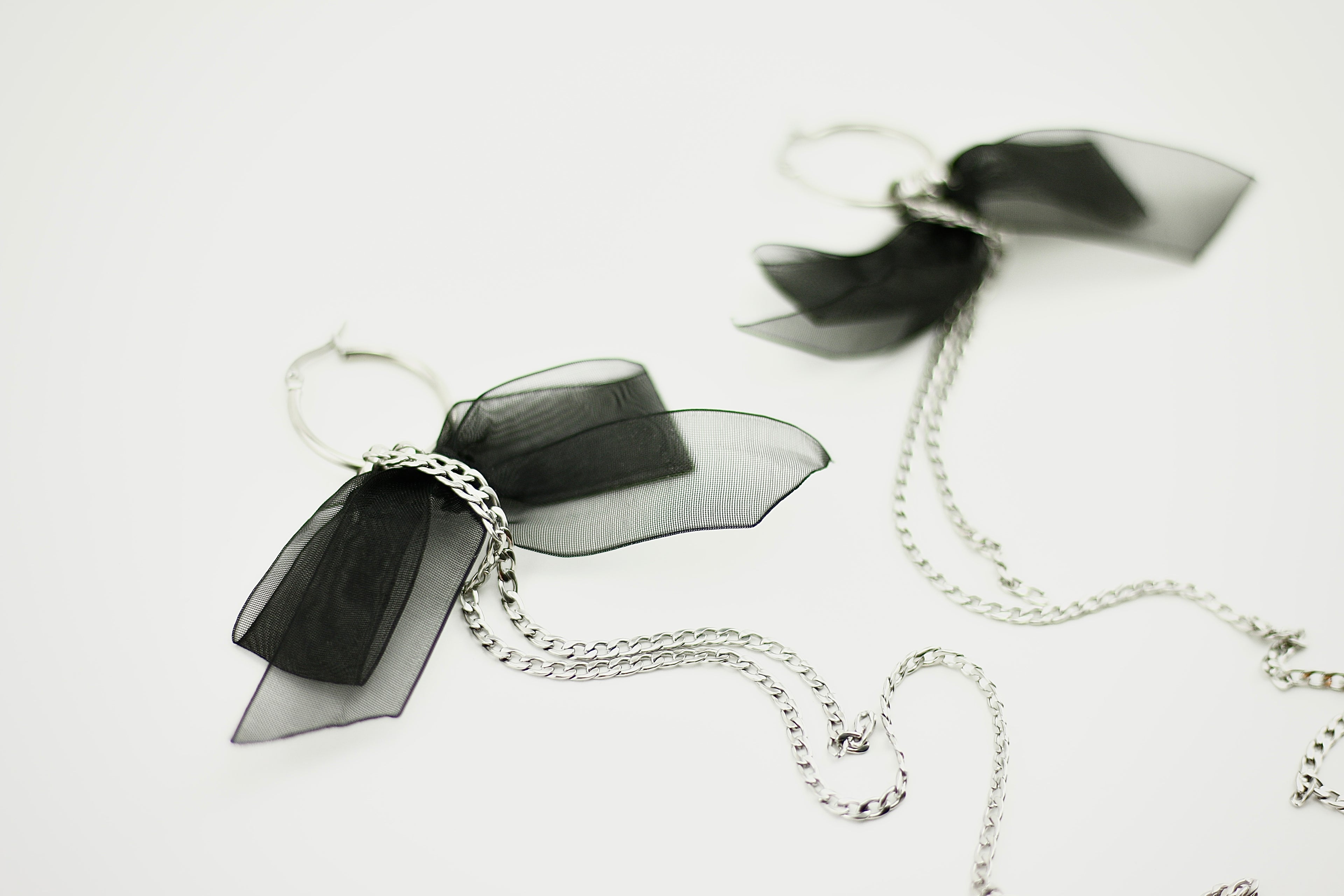 Black bow-shaped earrings with silver chains on a white background